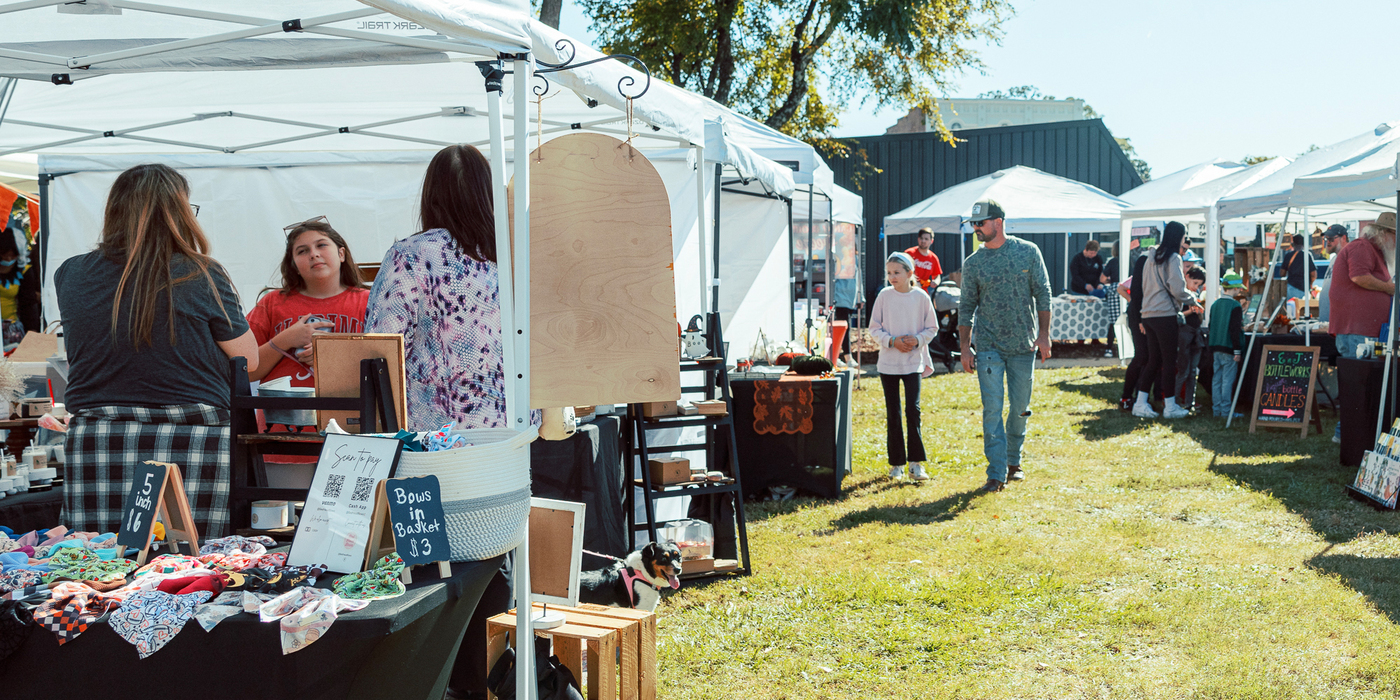 shoppers walking past vender tents in park